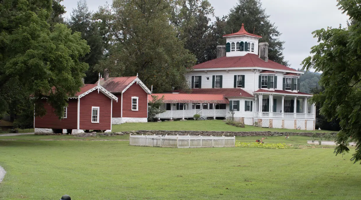 The white Italianate house at Hardman Farm with its red roof and rooftop cupola, red farm buildings beside it, on a wide lawn.