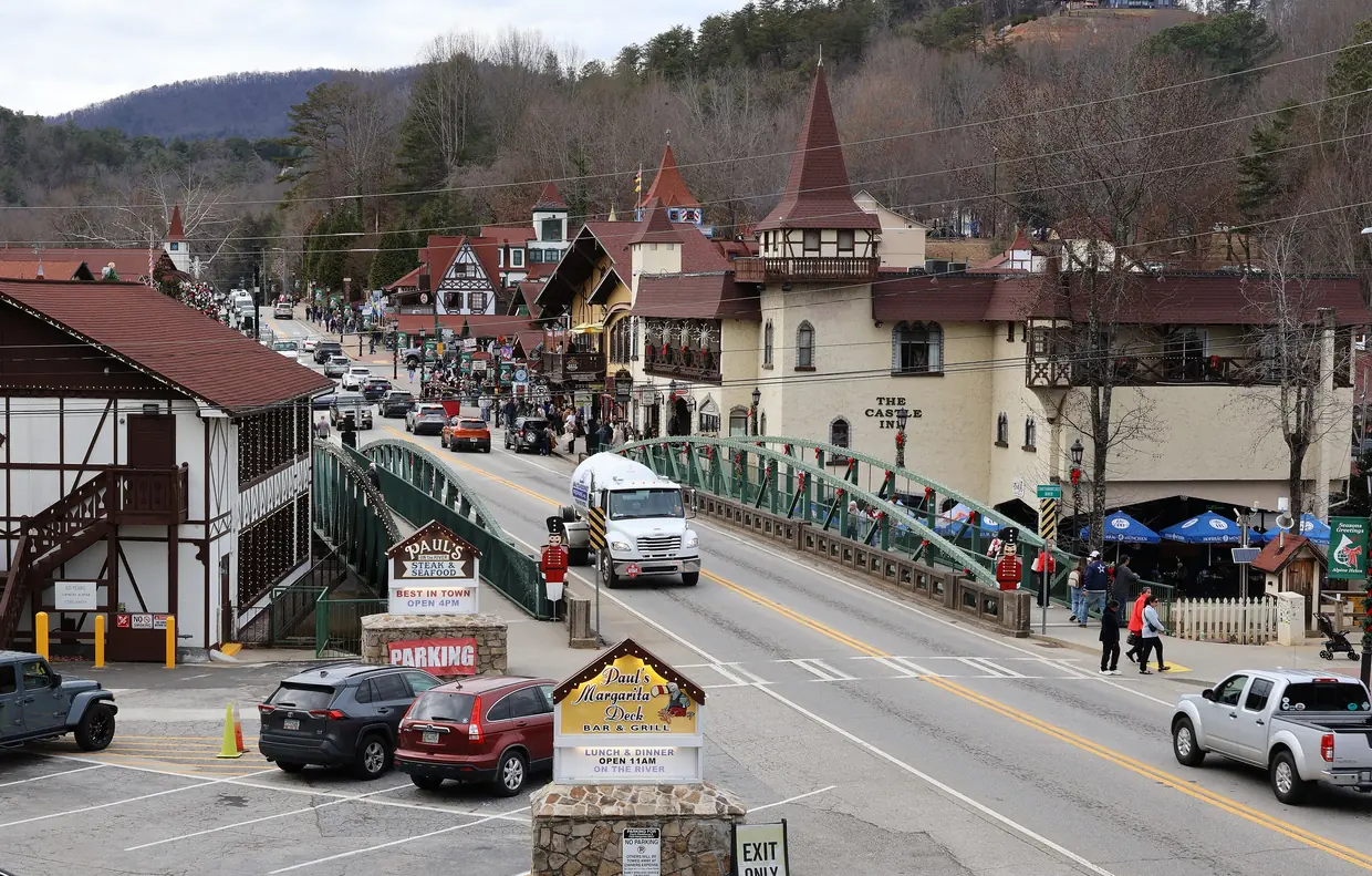 Downtown Helen on a grey December day: the green arched bridge over the Chattahoochee hung with garland and red bows, nutcracker figures at each end, The Castle Inn beside it and shoppers on Main Street.