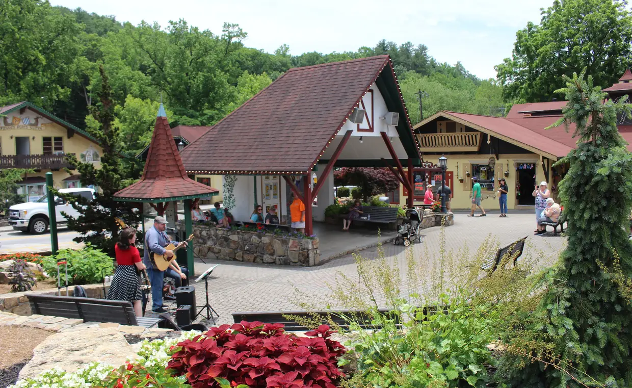 Two musicians playing on a brick plaza in downtown Helen beside a timber pavilion with a steep red roof, red poinsettias in front.