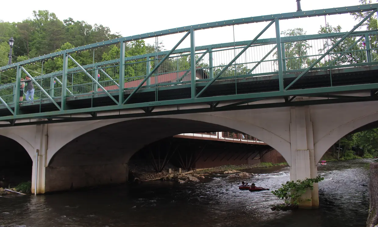 The Chattahoochee River running under the arched road bridge in Helen, with a green steel railing above and tubers on the water.
